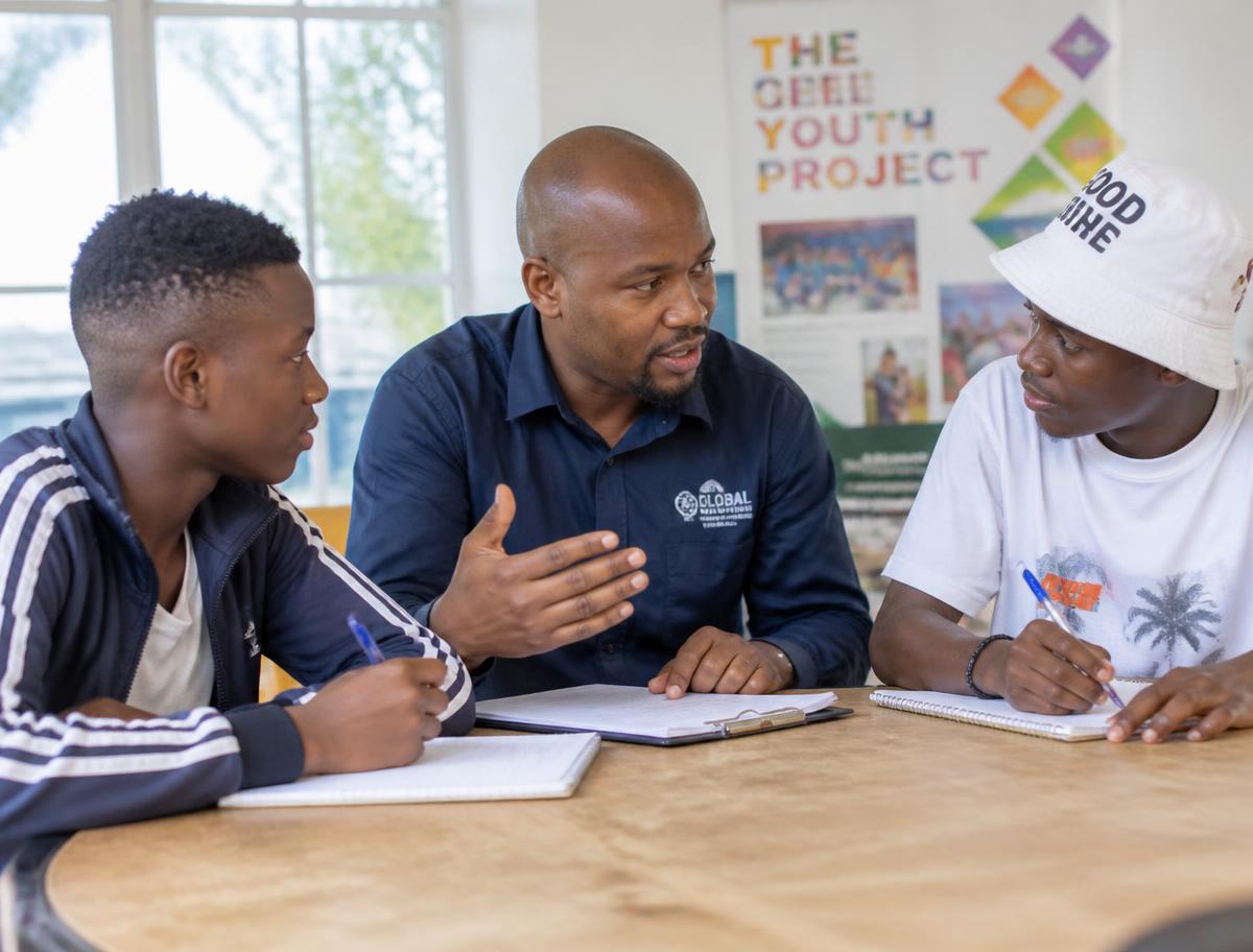 A mentor speaking with two young mentees around a table